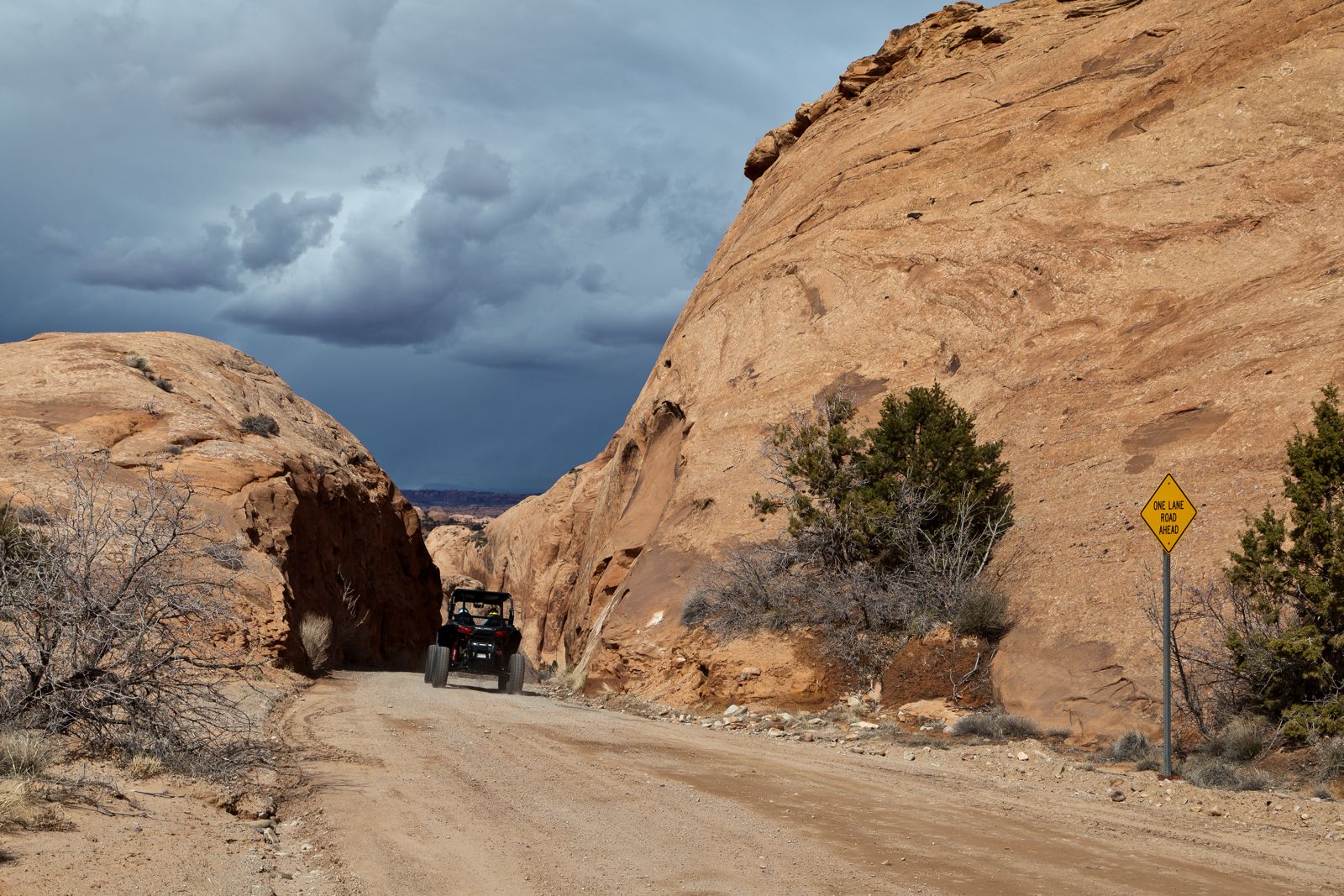 An off-road vehicle on a dirt road beside sandstone domes